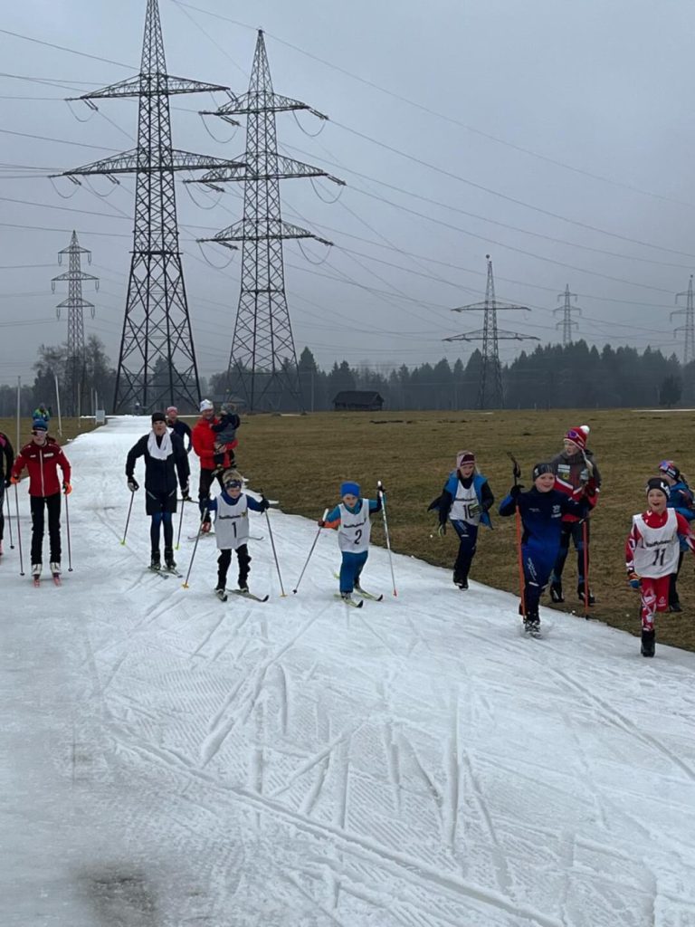 Kinder beim BC Langlauf auf der Schlossloipe Kaprun, umgeben von Wiesen und Strommasten.
